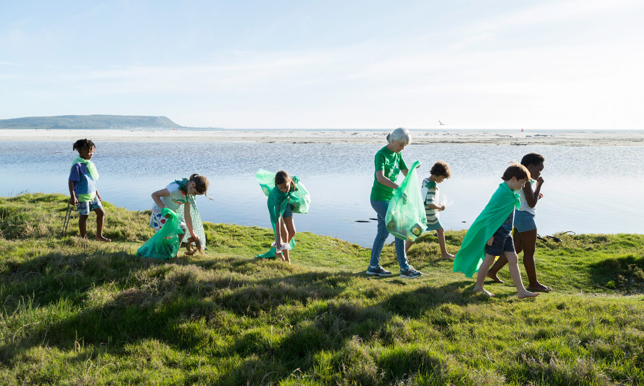 Six children, one lady, walking along the coast, carrying green bags and collecting rubbish