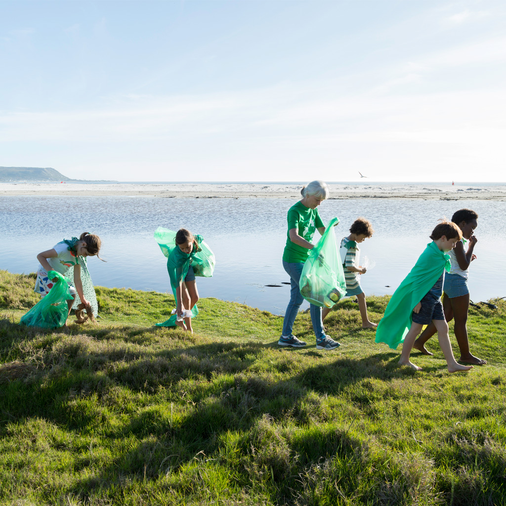Six children, one lady, walking along the coast, carrying green bags and collecting rubbish