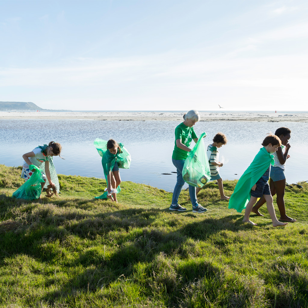 Six children, one lady, walking along the coast, carrying green bags and collecting rubbish Six children, one lady, walking along the coast, carrying green bags and collecting rubbish