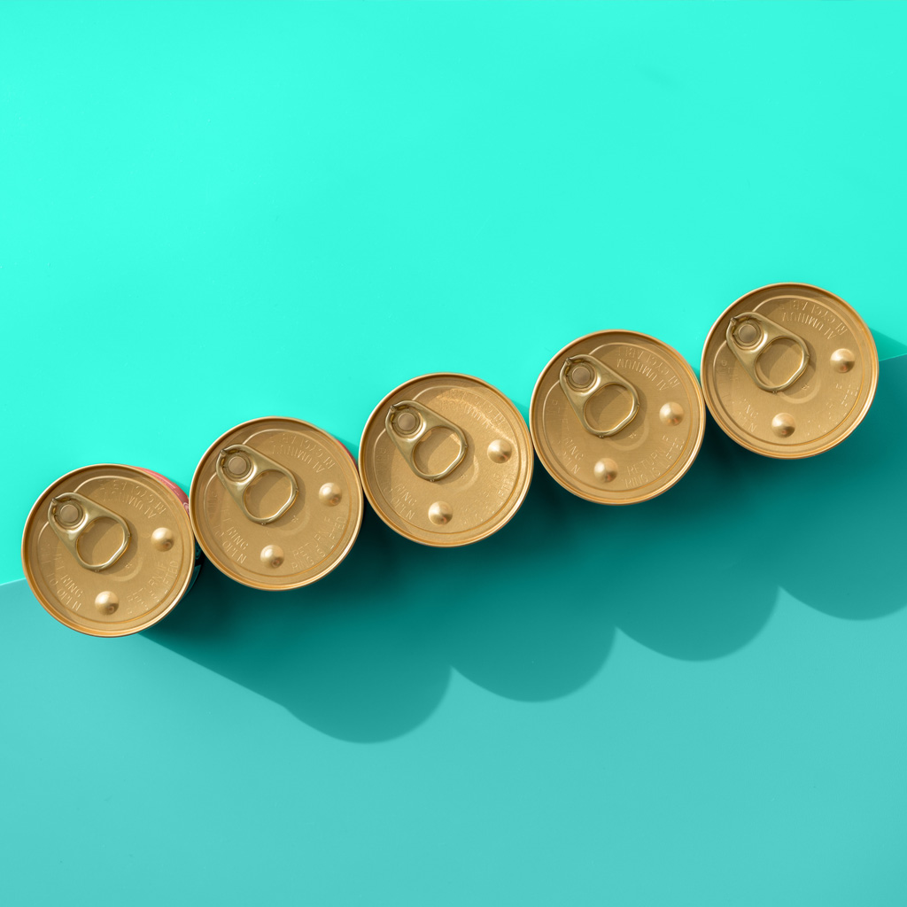Five gold cans side by side, from a bird's-eye view, on a blue and turquoise background Five gold cans side by side, from a bird's-eye view, on a blue and turquoise background