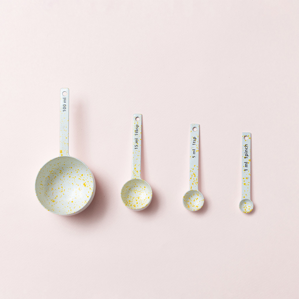 Four speckled measuring spoons, side by side, going down in descending order, on a pink background Four speckled measuring spoons, side by side, going down in descending order, on a pink background