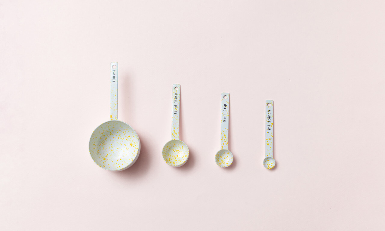 Four speckled measuring spoons, side by side, going down in descending order, on a pink background