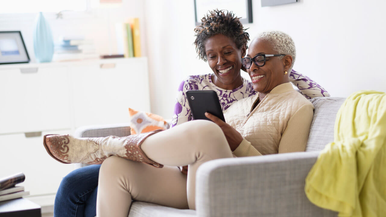 two woman sitting on a sofa, looking at a black ipad