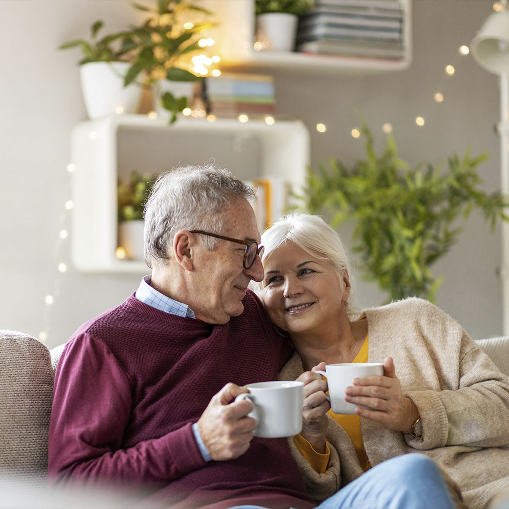 Older couple relaxing together on the sofa with cups of tea Older couple relaxing together on the sofa with cups of tea