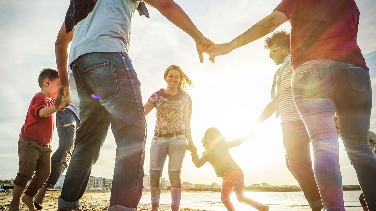 Circle of happy people playing together on the beach in the late afternoon